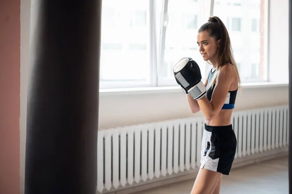 Hezká kickboxerka se připravuje na soutěže v boxerské hale, trénuje techniku úderů na boxovací pytel — Stock fotografie