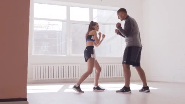 Un entraîneur expérimenté met la technique des coups à une jeune fille dans la salle de boxe — Video