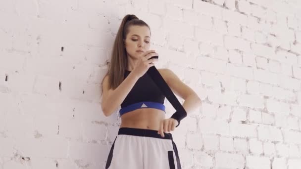 Una ragazza pugile contro un muro di mattoni bianchi avvolge una benda sportiva per la boxe sulle mani — Video Stock