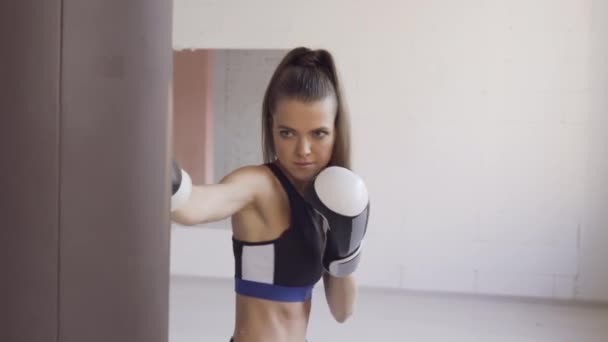 Een strenge trainer kijkt toe hoe zijn vrouwelijke kickbokser student een stomp op een bokszak oefent in een ruime trainingsruimte — Stockvideo