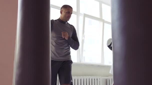 A pretty kickboxer girl is preparing for competitions with her coach in the boxing hall, practicing the technique of punches on a punching bag — Stock Video