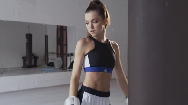 Retrato de uma jovem boxeadora atraente no ginásio usando luvas ao lado de um saco de perfuração — Vídeo de Stock