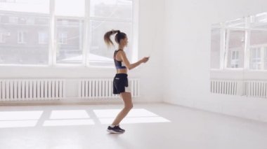 Spor salonunda ip atlayan ve gülümseyen, antrenmandan önce ısınan tatlı bir genç kız.