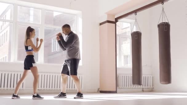 Un allenatore esperto mette la tecnica dei colpi ad una giovane ragazza nella sala da boxe — Video Stock