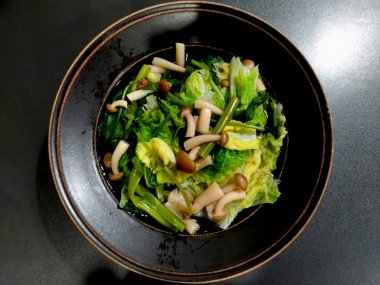 Sukiyaki siyah masa üzerinde siyah seramik kase içinde. mantar, beyaz lahana ve sabah zaferleri.