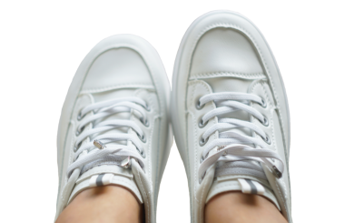 Beyaz bir arka planda, kızın ayağında beyaz spor ayakkabılar.