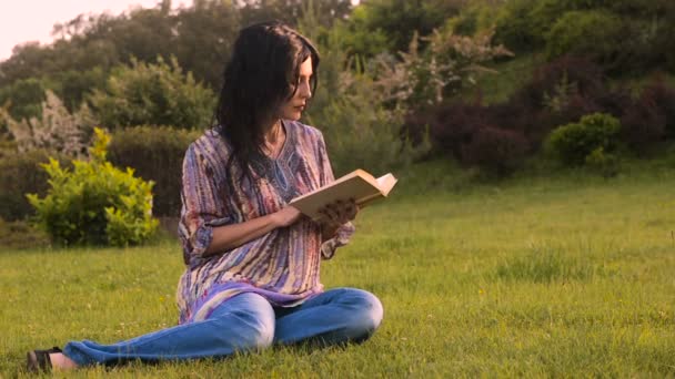 在公园春天的气氛中 一个年轻的黑发女郎读了这本书 放松了平静的气氛和周围的绿色植物 — 图库视频影像