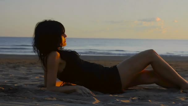 女人引诱和愉快地滚动沿着沙滩上的沙子 轻轻地笑 从邻近地区 可以看到海和日落的环境 — 图库视频影像