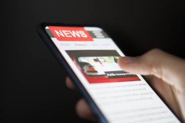 Ekranda haber olan cep telefonu tutan bir adam. Gazete 