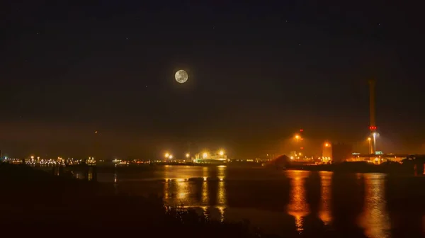 View of cargo port at night . View of the loading in the sea port  . Cargo area on night time with reflections on water  . eclipse of the moon