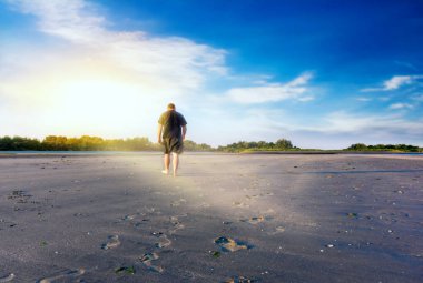 Sahada yürüyen genç adam. Yeni yükseliş. Gökten gelen ışık. Güneş doğarken dua . 