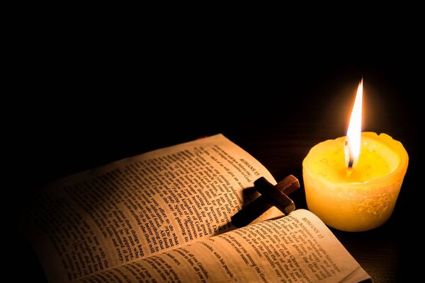 Burning candle and Bible . The psalms . Holy book . told in the Bible's New Testament , on a black background . Christian cross .
