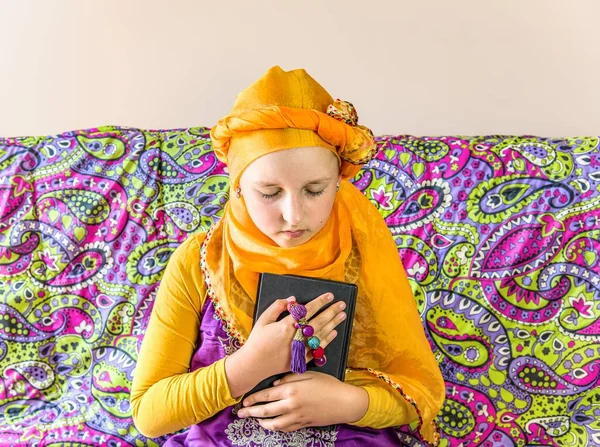 Muslim girl prays at home alone . child girl reads prayer book . background of regia teachings