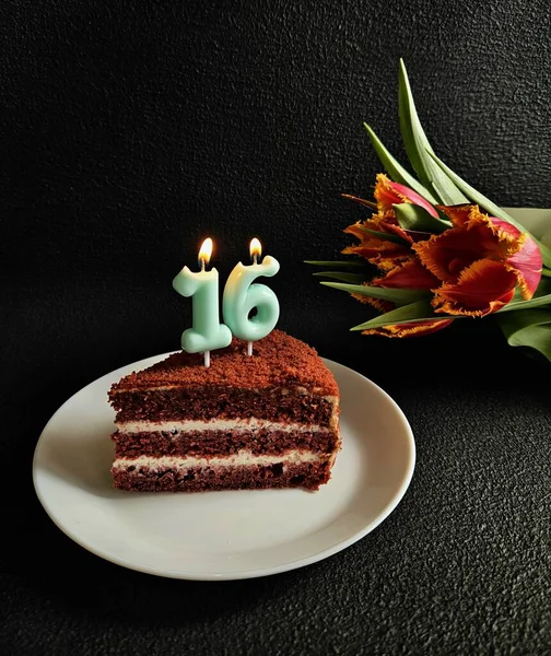 birthday cake on a black background. the concept of birthday, a cake and a birthday card. piece of birthday  cake with candles with beautiful flowers on the background.16 years