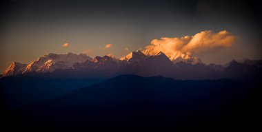 Karla kaplı görkemli dağ zirveleri gün batımının altın sarısı renklerinde güneşlenir. Karanlık önplan manzarasıyla güzel bir tezat oluşturur ve doğanın dingin ama güçlü güzelliğinin altını çizer..