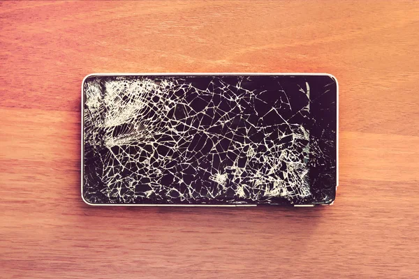 Smartphone mobile with a broken screen. Background wood