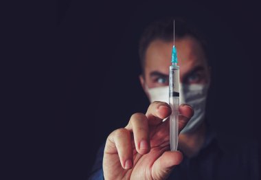 Kızgın doktor kadın tıbbi maskeli bir şırınga bir izole koyu arka plan üzerinde tutar. kötü doktor. Vasıfsız tıp. kötü doktor. çılgın, deli, deli, deli, deli, deli,