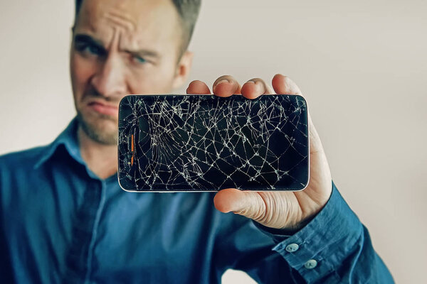 The guy is holding a black smartphone with a broken display. Broken screen of modern frameless phone. a large crack in the form of a web on the smartphone screen close-up.
