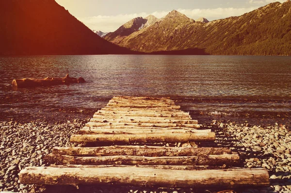 Old Wooden pier on the lake. Long exposure. Landscape view with wood bridge in Lake and Mountain background. Wooden pier on the lake. log wooden bridge on a background of lake and mountains