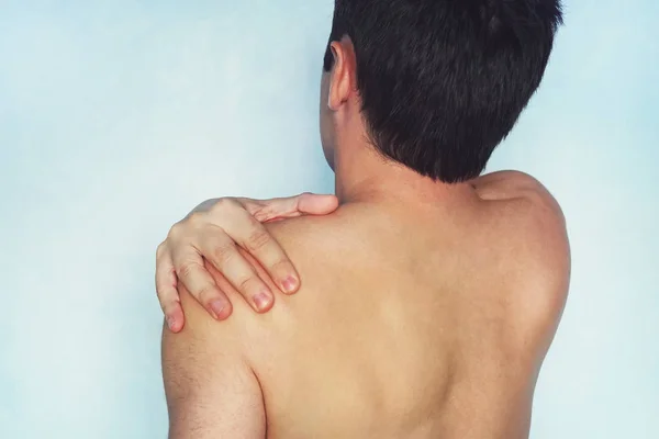 A man who has a shoulder pain. low back pain. A young guy with a naked body holds his arm a sore shoulder on a blue background. athlete with a fracture or dislocation of the shoulder.