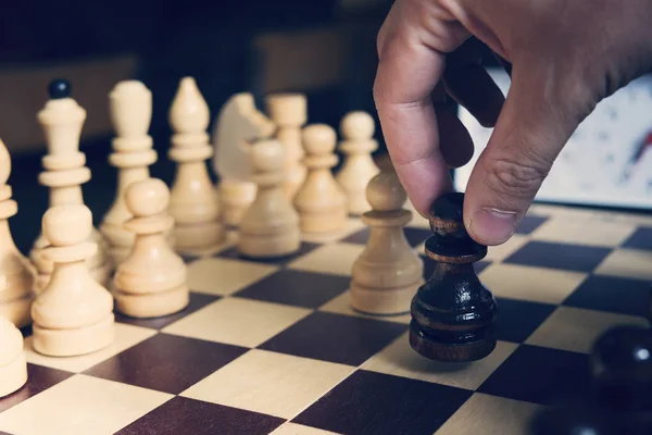 male hand playing chess on light blurred background , black pawn in the hand of the beginning of a game of chess