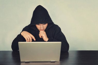 Siyah hacker uzun kollu gömlek laptop ve düşünme somethings önünde masaya oturan siyah maskeli. Laptop bakıyor. Görüntü arka plan bir makinedir