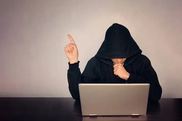 Hacker hooded in front of his computer show finger. Dark face. hooded .technology concept, hacker points finger at empty space for text