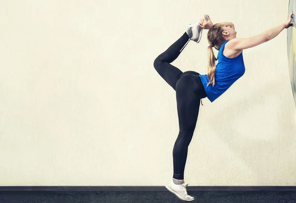 Pretty blonde woman with slim body stand in yoga pose with one leg raised up. Gymnastic pose vertical