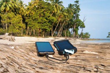 Alternatif enerji kaynağı. Pil güneş enerjisi ile doludur. Hareket eden aygıt içinde belgili tanımlık vahşi şarj. Island beach. Powerbank palmiye ağaçları ve kumlu plaj arka plan üzerinde telefon ücretleri
