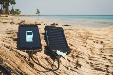 Alternatif enerji kaynağı. Pil güneş enerjisi ile doludur. Hareket eden aygıt içinde belgili tanımlık vahşi şarj. Island beach. Powerbank palmiye ağaçları ve kumlu plaj arka plan üzerinde telefon ücretleri