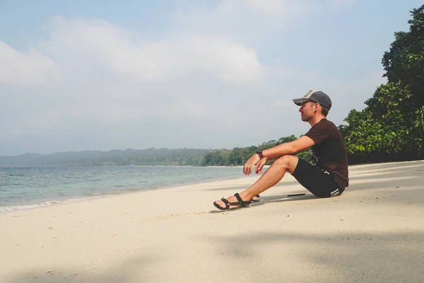Ένας Νεαρός Άντρας Κάθεται Μια Λευκή Αμμώδη Παραλία Και Κοιτάζει — Φωτογραφία Αρχείου