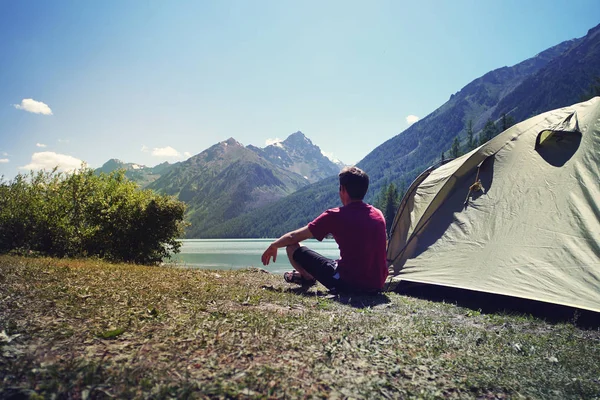Alleinreisende Menschen reisen in der Nähe des Sees, reisen allein. junger Tourist sitzt hinter einem grünen Zelt und blickt auf eine wunderschöne Berglandschaft mit einem See. — Stockfoto
