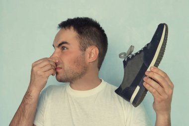 Bir adam elinde tuttuğu spor ayakkabısından yayılan koku yüzünden burun deliklerini sıkıyor..