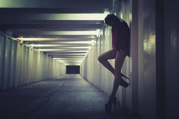 Una prostituta que trabaja en la calle nocturna. sexy chica de pie en la pared en el túnel doblando su pierna en una pose seductora — Foto de Stock
