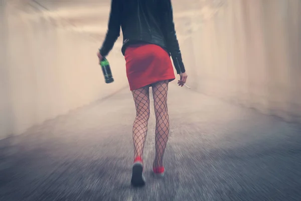 Drunk woman with cigarette and bottle goes into distance along corridor stumbling and falling. Young girl in red skirt tights walk away. concept alcoholism bad habits. Blur effect showing dizziness — Stock Photo, Image