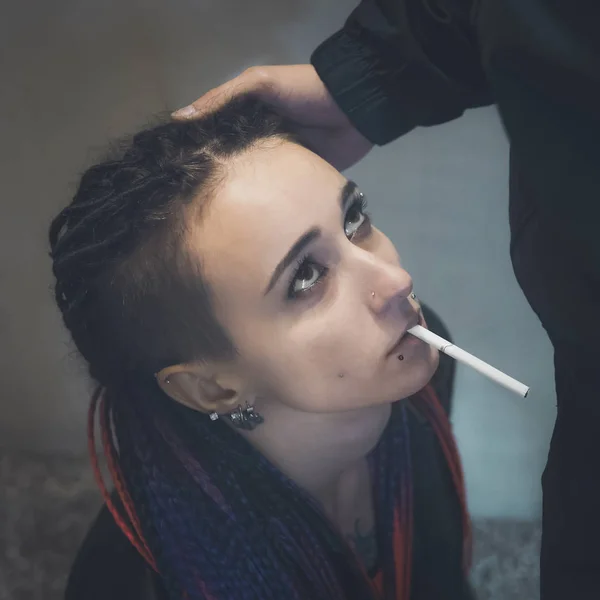 Una chica con un cigarrillo en la boca se arrodilla delante de un hombre y mira hacia arriba con una mirada quejumbrosa. Publicidad social anti tabaco. El concepto de dependencia de los esclavos de la nicotina — Foto de Stock