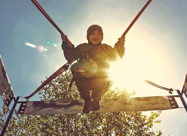 Cheerful cute little boy jumping on a trampoline against the blue Sunny sky like flying in the sky