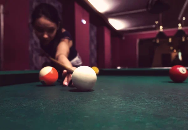 Young beautiful young lady aiming to take the snooker shot while leaning over the table in a club. Girl playing Pool billiard