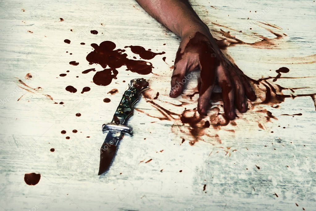 Conceptual image of a victim hand holding a sharp knife with blood on it resting on a white vintage floor. Concept photo of murder and crime