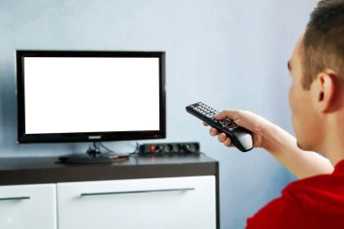TV uzaktan kumandası geniş ekran televizyonun önünde mavi duvar arkasında boş ekran var. Genç adam televizyonun kumandasını değiştiriyor..