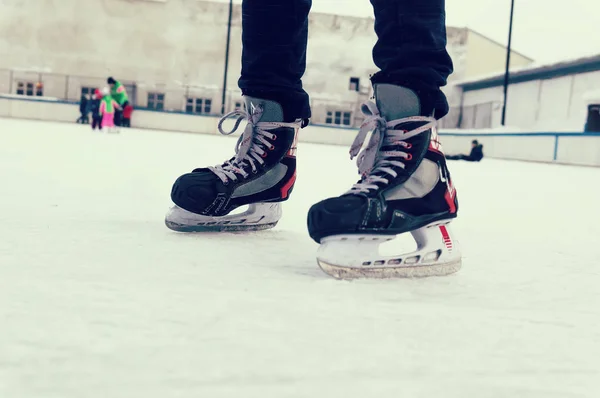 feet on the skates of a person rolling on the ice rink on the background of the ice rink in the open air. old sports hockey skates. on a man's leg. place for text,