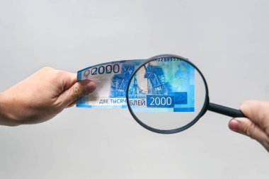 Rus para birimi, yeni 2000 Rublesi faturaları da dahil olmak üzere. Erkekler ellerini 2000 ruble ve büyüteç tutun. Rus banknot Orijinallik doğrulama