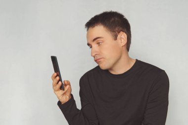 Genç bir adam siyah bir akıllı telefon ekranında yüzünde küçümseyen bir duygu ile görünüyor. ilginç yazışmalar. sıkıcı ki. resim, fotoğraf, fotoğraf, resim,