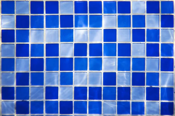 Square pattern of blue and light blue tiles for bath walls and floor design or swimming pool design. Water blinks on tiled walls in a water park. Indoor pool ground design. Clear swimming pool water.