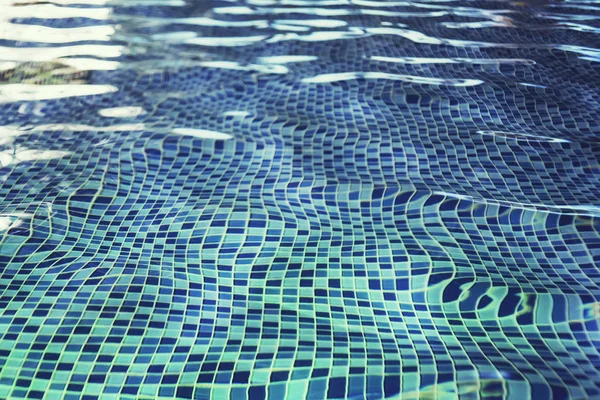 A fish eye effect of indoor pool rippling water at the blue-tiled mosaic floor. Waving of clean water in swimming pool with tiled floor. Swinging of water in shallow pool. Mosaic tiles under water.
