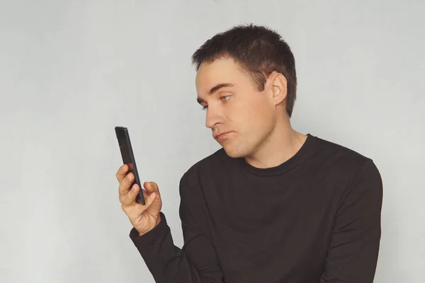 Young Guy Looks Screen Black Smartphone Dismissive Emotion His Face — Stock Photo, Image