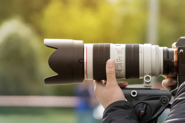 Handshot of a professional photographer outdoors. Man holds a modern camera device. Cameraman shoots outdoors. Shooting with lens. Paparazzi with high-end optical objective. Photographic equipment.