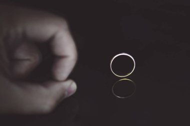 Close up of man's fingers on the reflecting black surface pushing on the wedding ring at the black background. Male hand on the black table near the gold ring set edgewise. Man put ring off. Divorce clipart