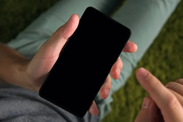 Primer plano de un joven usando el teléfono inteligente con la pantalla en negro. La persona está en línea desde un teléfono inteligente. El hombre sostiene un teléfono y levanta el dedo índice derecho para tocar la pantalla. Montaje de pantalla en blanco . — Foto de Stock