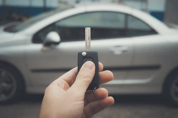 Male hand holding car keys with car on background. Man uses remote vehicle key to lock the car. Driver has parked the car. Automobile buying tricks. Driver unlocks its vehicle by remote control.